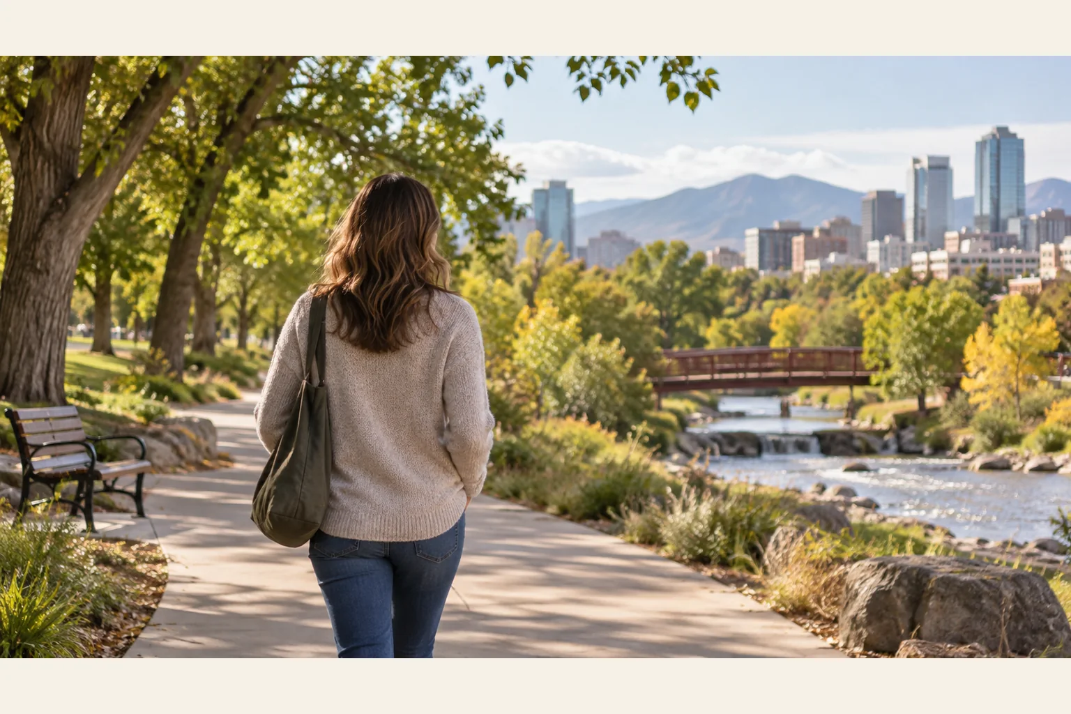 Illustrative scene: Quiet Walk Along a Riverside Path Near the City Illustrative scene: A person carrying a shoulder bag walks along a tree-lined riverside path with a bridge, city skyline, and mountains ahead.