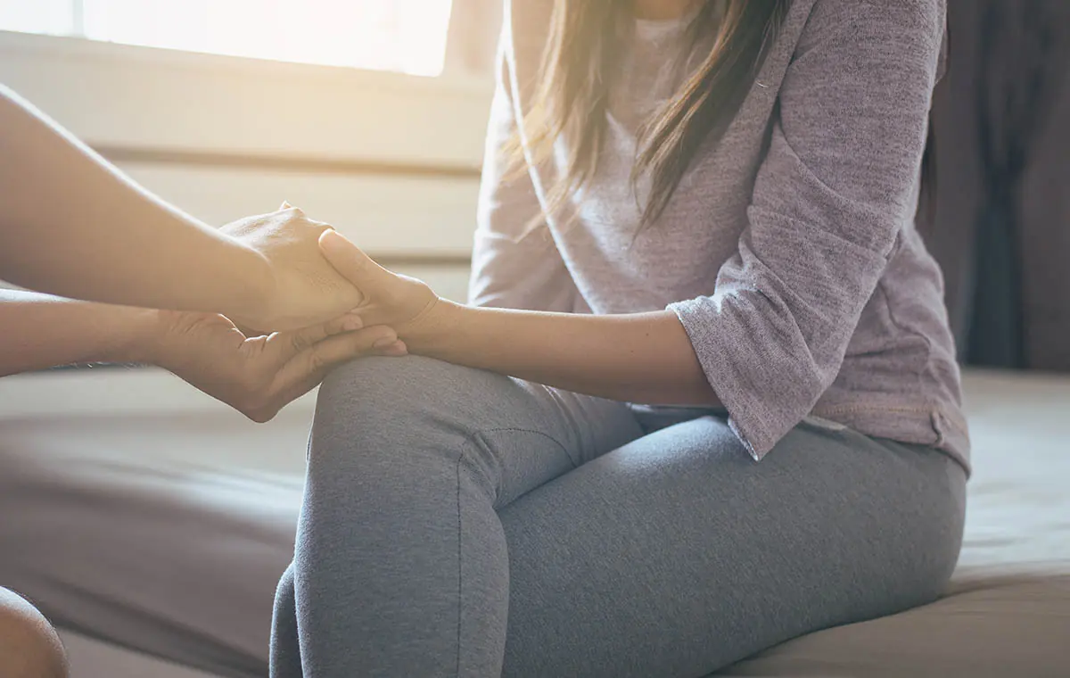 person comforting woman seated on bed telling her about trans women addiction resources
