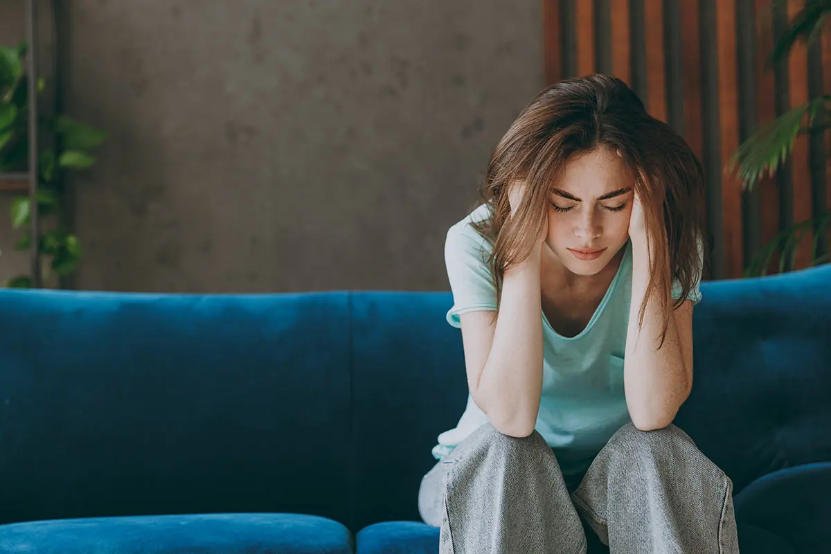 young woman sitting on couch with her head in her hands wondering about the difference between meth vs adderall