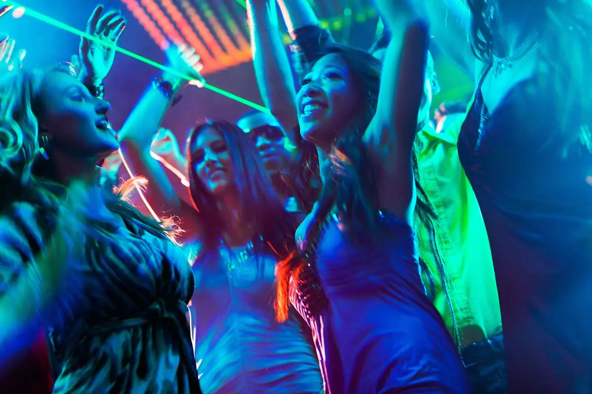 two young women dancing and smiling in a crowded club about to learn the truth behind molly and club drug addiction