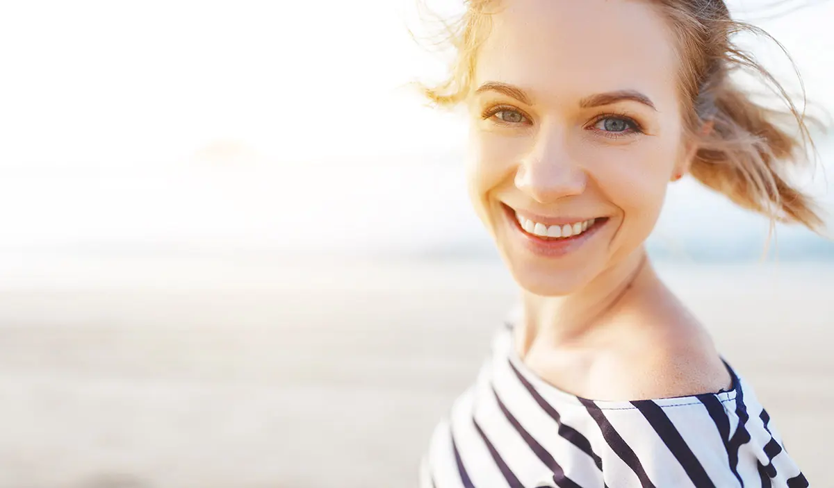 young woman smiling and walking on beach realizing the importance of womens addiction treatment
