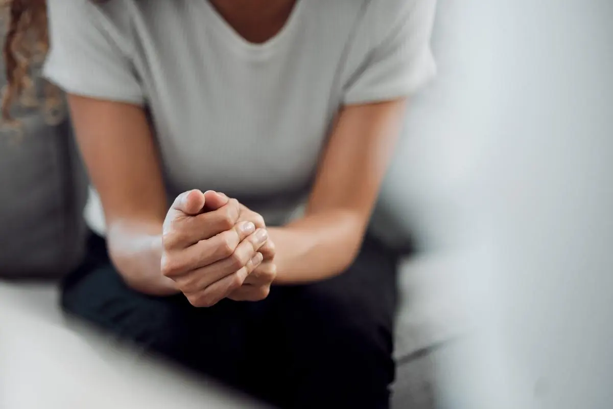 young woman seated pensively on a couch clutchinhg her hands together nad wondering do I need treatment and the importance of getting professional help.