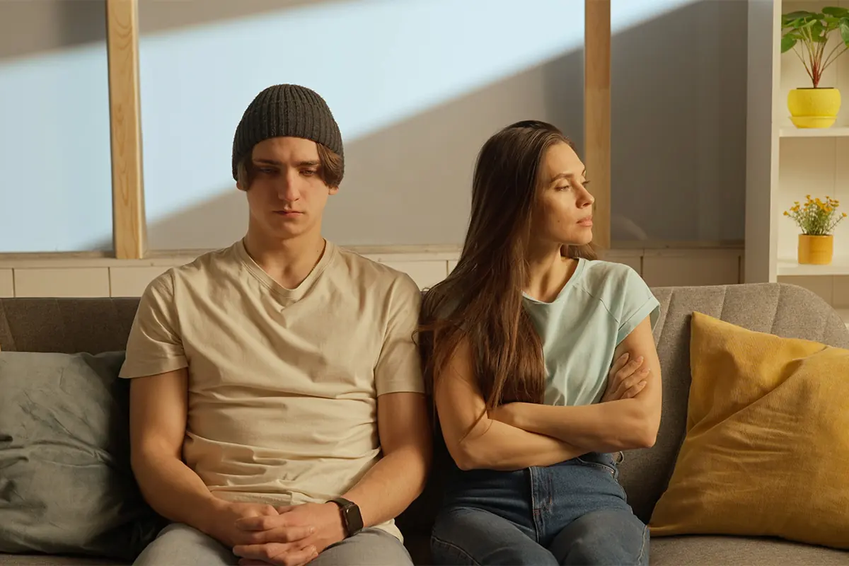 couple seated on couch with irate woman looking away from subdued looking man wondering do women get addicted to alcohol faster than men