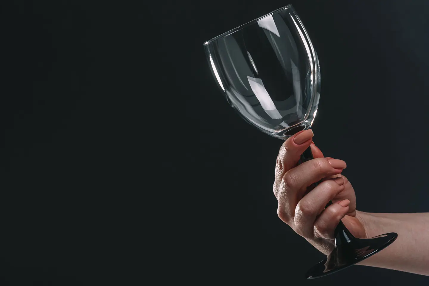 woman holding out an empty wine glass and staring at it as she asks herself, "Why can't I stop drinking?"
