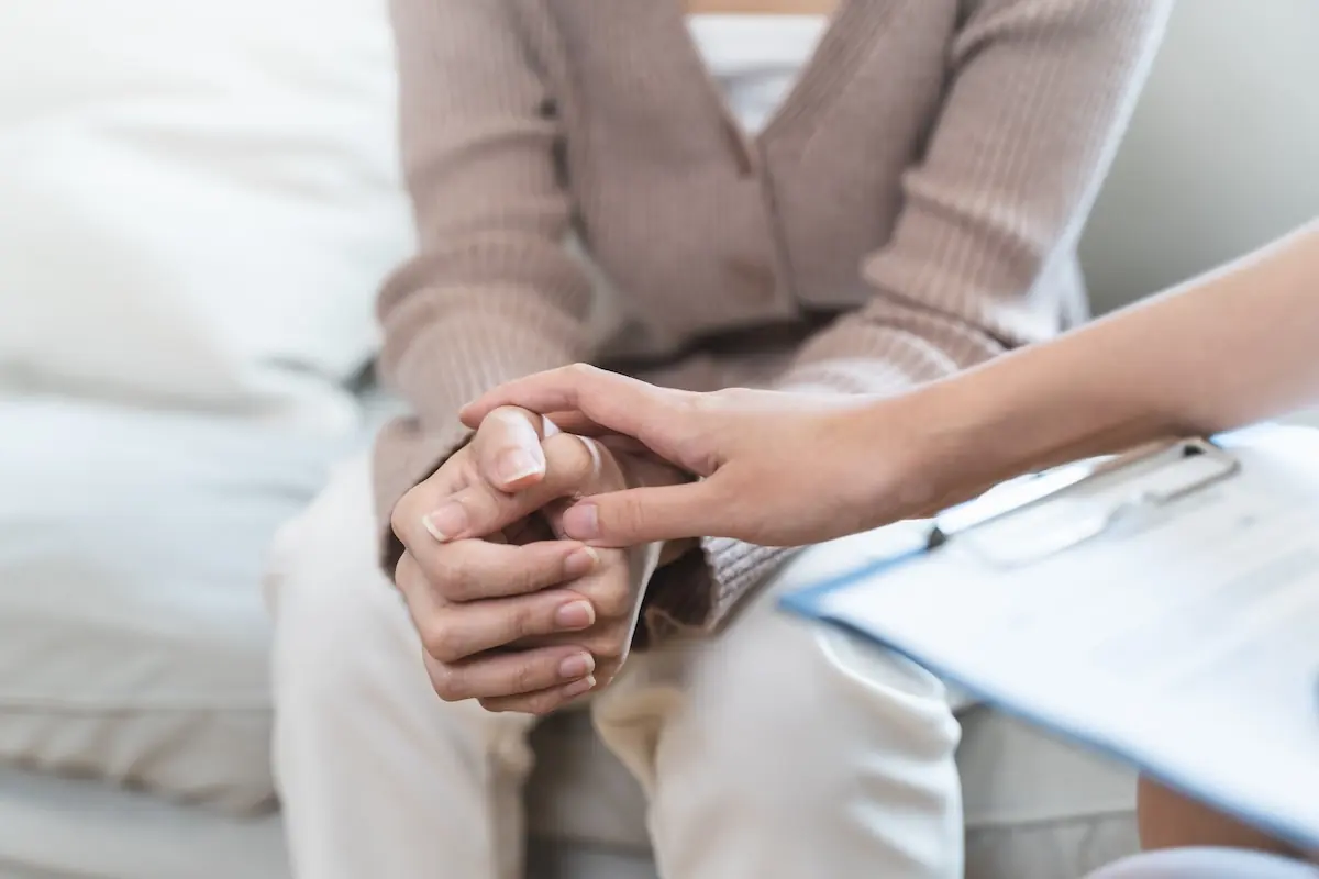 Person offering comfort by gently holding another person’s hands during a conversation.