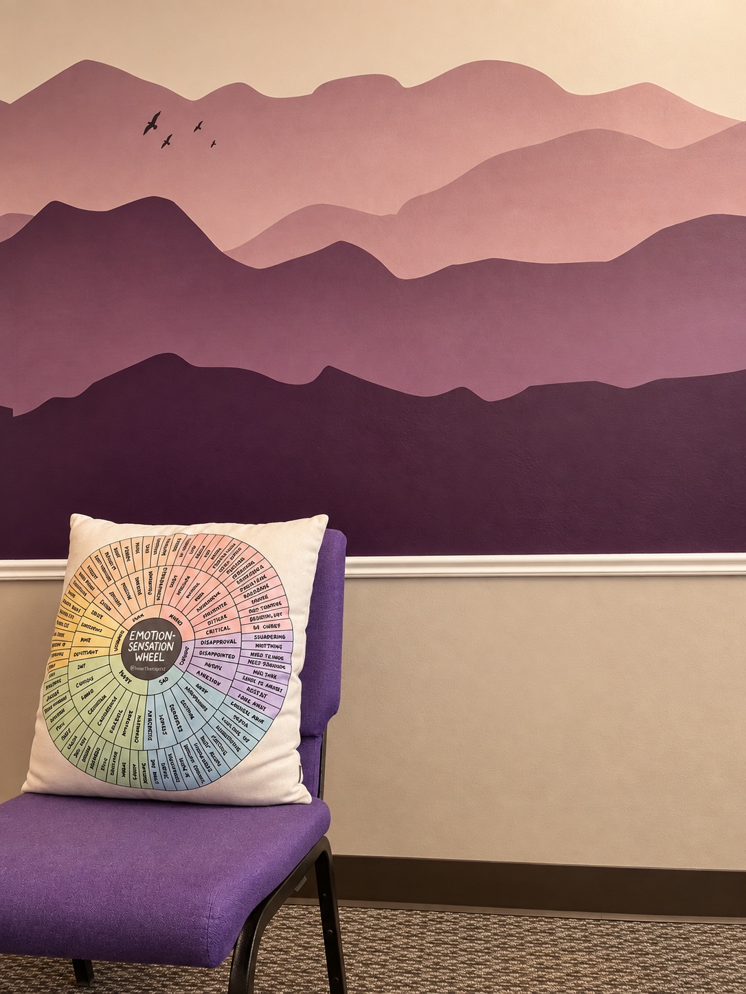 Purple chair beside a mountain mural and emotion-wheel cushion