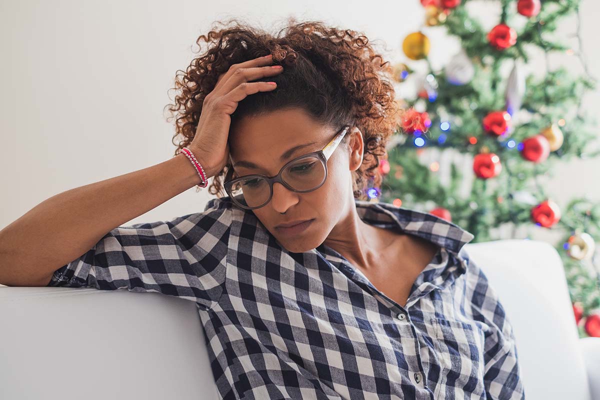 Avoid Stress, Depression, & Relapse This Holiday agitated women sitting on couch with head in her hands trying to avoid stress, depression, and relapse this holiday season