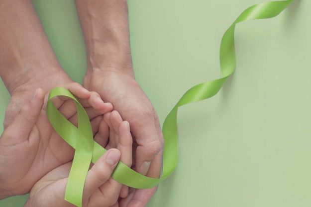 Adult and child hands holding Lime Green Ribbon on green backgro a green ribbon symbolizes world mental health day in october