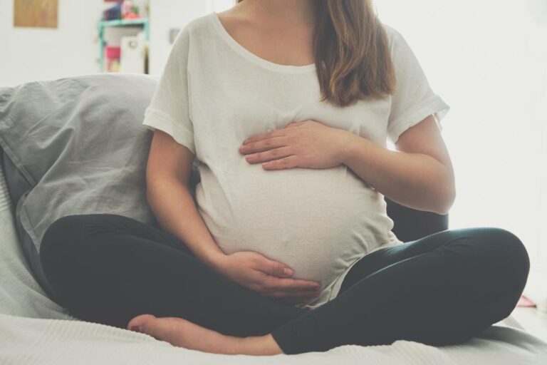 pregnant woman seated on her bed holding her swollen belly wondering what are the risks of taking Rivotril during pregnancy