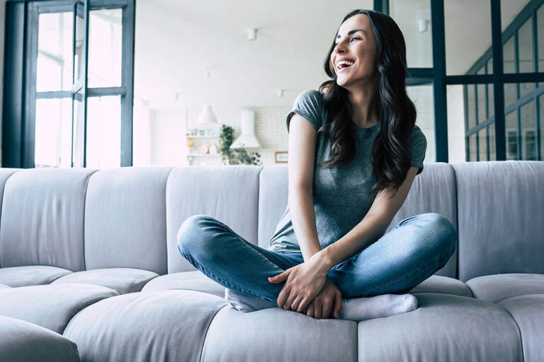 young woman sitting on couch and smiling while enjoying sober living in denver