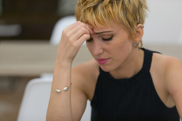 young woman looking concerned and holding her head in her hands as she attempts to determine what are the signs and effects of date rape drugs