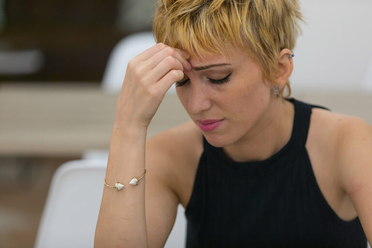 What Are the Signs & Effects of Date Rape Drugs young woman looking concerned and holding her head in her hands as she attempts to determine what are the signs and effects of date rape drugs