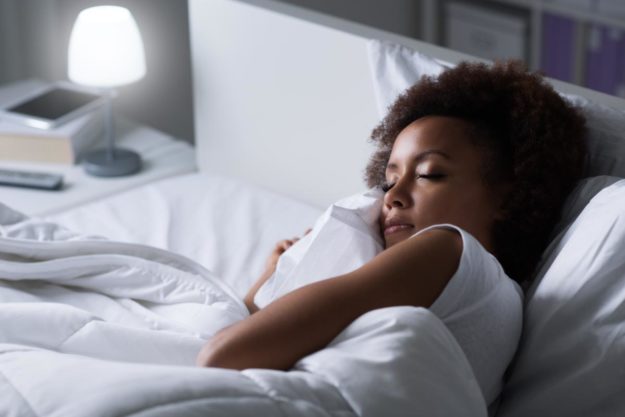 3 Natural Alternatives to Sleeping Pills young woman in bed with table lamp on trying to sleep and wishing she had 3 natural alternatives to sleeping pills