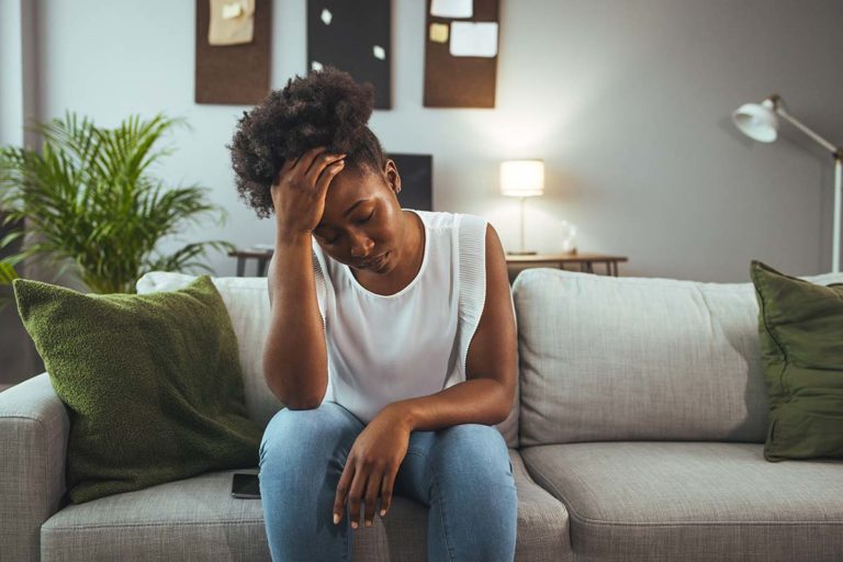 a woman holds her head on a couch struggling with women's mental health issues