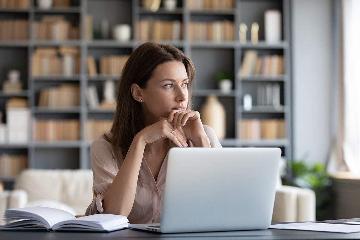 serious looking woman staring into the distance while sitting in front of open laptop researching the 5 subtle signs of gray area drinking