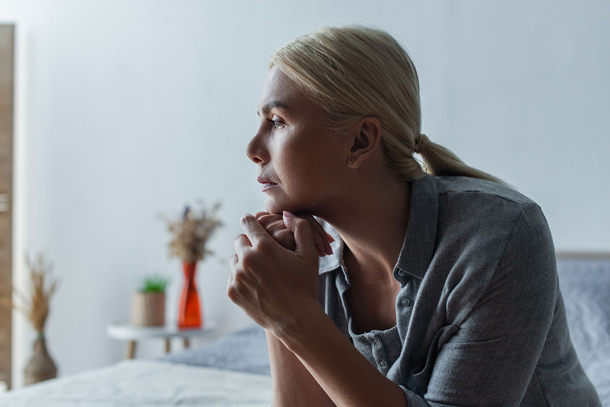 woman sitting on her bed lost in thought as she attempts to understand the symptoms for alcohol withdrawal in women