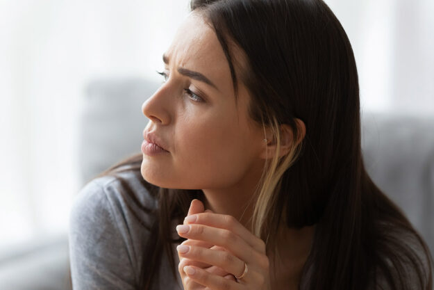 5 Strategies for Women to Help Manage Stress close up of young woman sitting at home with a serious expression as she considers one of 5 strategies for women to help manage stress