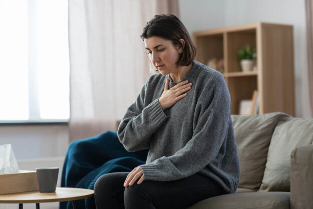 woman seated in professional office holding hand to her chest as if in pain and experiencing one of 5 physical symptoms of anxiety in women