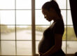 pregnant woman standing in front of window cradling stomach and worried about the dangerous effects of maternal cocaine use