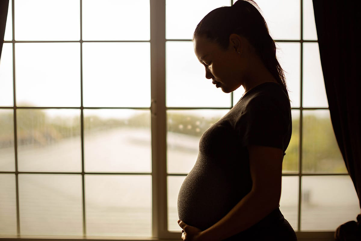 pregnant woman standing in front of window cradling stomach and worried about the dangerous effects of maternal cocaine use