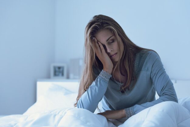Are There Withdrawals from Sleeping Pills young woman seated in bed and looking unwell wondering are there withdrawals from sleeping pills