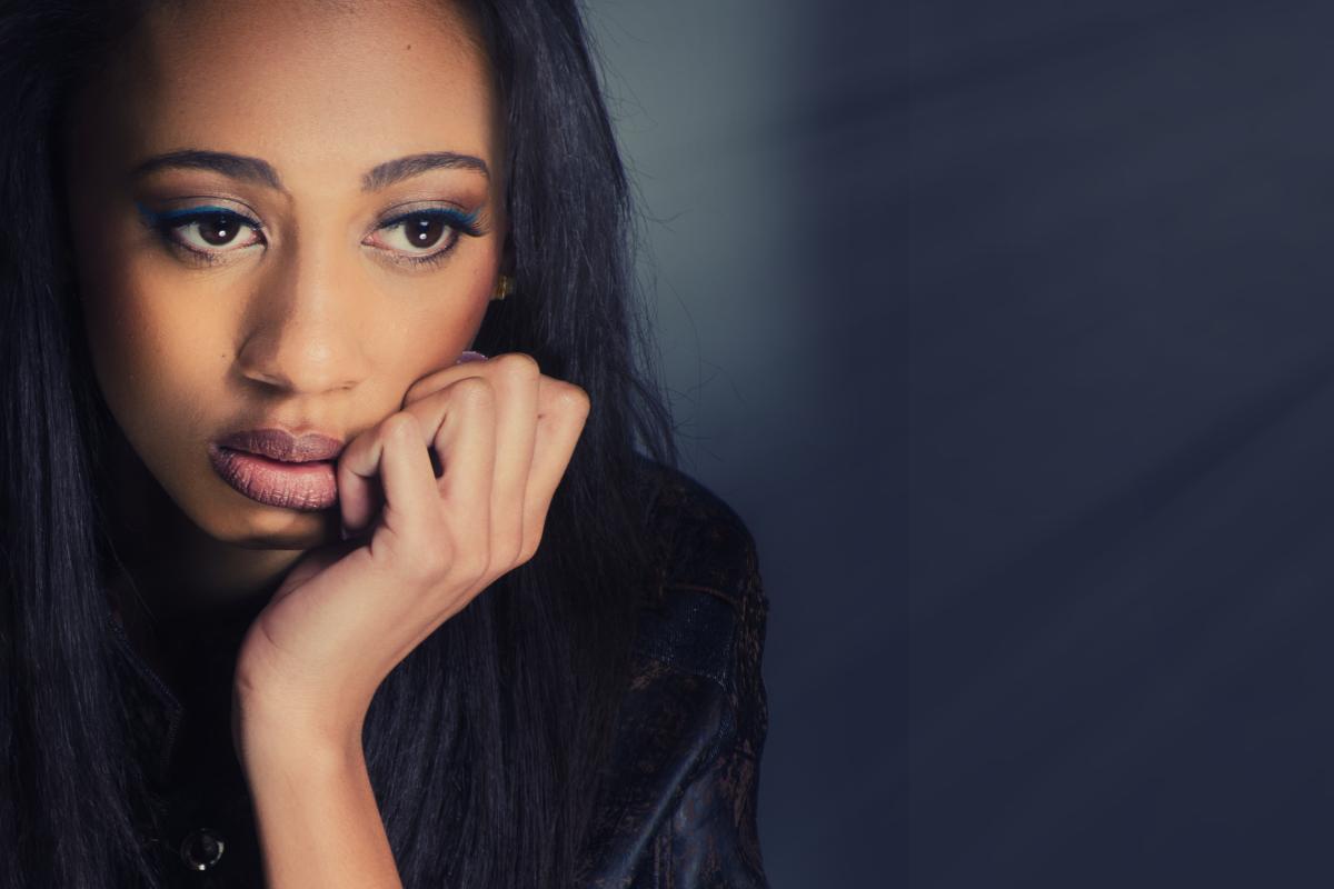 pensive looking woman in dimly lit room ponders the dangers of mixing Wellbutrin and alcohol