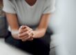 young woman seated pensively on a couch clutchinhg her hands together nad wondering do I need rehab and the importance of getting professional help.