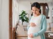 pregnant woman standing in her home holding her belly and pondering safe detox and the fastest way to clean your system during pregnancy.