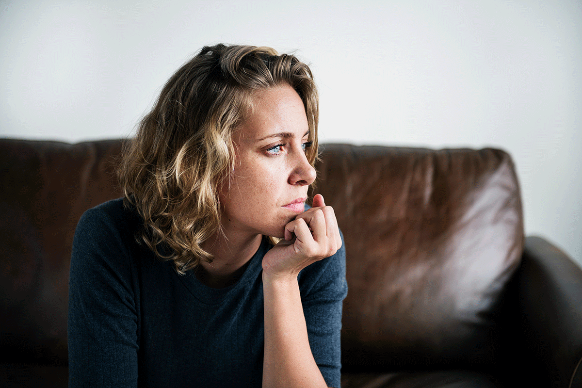 young woman seated on couch deep in thought as she ponders what stops people from getting mental health treatment.