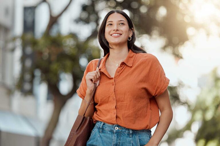 young woman smiling as she walks outside on a sunny day after practicing 3 self-care tips for mental health