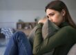 young woman seated on couch hugging a pillow to hear chest and looking pensive as she contemplates what is obsessive-compulsive disorder?