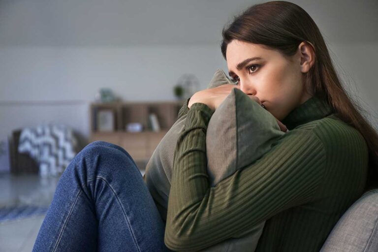 young woman seated on couch hugging a pillow to hear chest and looking pensive as she contemplates what is obsessive-compulsive disorder?