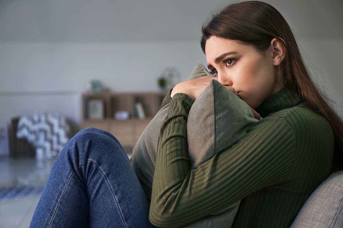 What-Is-Obsessive-Compulsive-Disorder- young woman seated on couch hugging a pillow to hear chest and looking pensive as she contemplates what is obsessive-compulsive disorder?