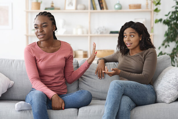 Alcoholic Sister in Denial- What to Do When a Loved One Refuses Help Two sisters seated on couch as one struggles to help her alcoholic sister in denial who is refusing help by offering treatment options