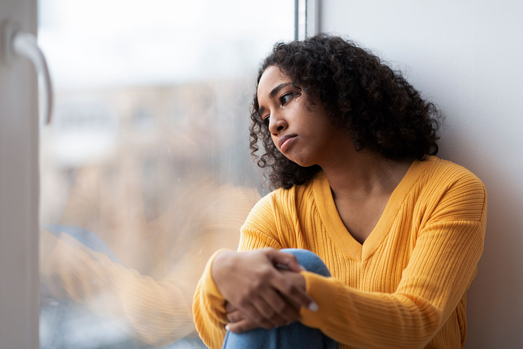 Do Women Get PTSD More Than Men – Women’s Recovery CO A woman leans against a window. She is experiencing symptoms of PTSD in women.