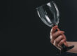 woman holding out an empty wine glass and staring at it as she asks herself, "Why can't I stop drinking?"