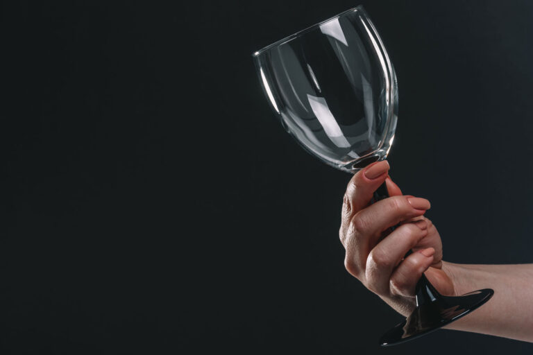 woman holding out an empty wine glass and staring at it as she asks herself, "Why can't I stop drinking?"